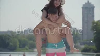快乐的年轻夫妇在海滩上玩得很开心。 那个女孩坐在一个男人的背上微笑。 情侣们在附近<strong>享受</strong>周末<strong>时光</strong>